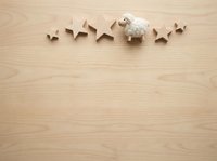Wooden stars and fluffy sheep toy arranged on light wood surface, overhead flat lay composition for nursery, children's design, and holiday creative projects.