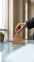 Businessman placing wooden block with gear symbol on pyramid stack, representing business growth, strategy and organizational development in modern office setting.