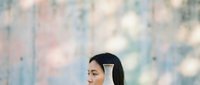Young Asian woman wearing white wireless headphones listening to music with peaceful expression against soft pastel bokeh background for relaxation content.