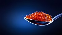 Fresh red caviar on silver spoon against dark blue background, luxury seafood delicacy with translucent salmon roe pearls in dramatic lighting.