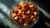 Fresh strawberries and pineapple chunks mixed in crystal glass bowl on dark background with dramatic lighting, ready to serve healthy fruit salad.