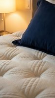 Cozy bedroom interior with navy blue pillow on cream quilted bedding, warm lamp lighting creating relaxing ambiance for sleep, rest, and home decor design.