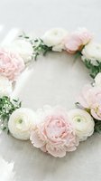 Delicate floral wreath with soft pink peonies and white ranunculus flowers arranged in circle on neutral linen background for wedding and spring decor.