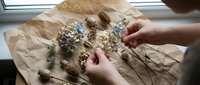 Hands arranging dried herbs and flowers on kraft paper for culinary, medicinal, or craft projects and herbal preparations.
