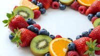 Fresh mixed fruits arranged in circle on white background with strawberries, blueberries, kiwi, orange slices creating colorful frame for healthy eating concepts.