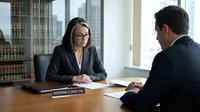 Professional female lawyer in glasses consulting with male client in modern law office conference room for legal advice and representation services.