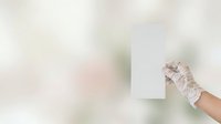 Hand wearing white lace glove holding blank white card against soft blurred background, suitable for wedding invitations, greeting cards, and elegant event announcements.