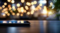Smartphone on wooden surface with blurred festive bokeh lights and pine branch in background creating magical holiday atmosphere.