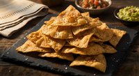 Golden corn tortilla chips arranged on dark slate board with salsa and guacamole bowls, perfect for Mexican cuisine appetizers and snack presentations.