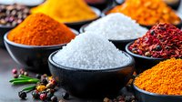 Colorful aromatic spices and seasonings in black ceramic bowls on dark background, including sea salt, turmeric, paprika and dried chili peppers for cooking.