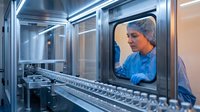 Female scientist in protective gear working with pharmaceutical manufacturing equipment in sterile laboratory environment for drug production.
