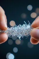 Fingers holding delicate crystalline silver structure against dark background with bokeh lights, showing microscopic detail of metallic dendrites growth.