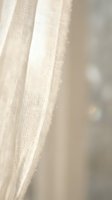Soft natural linen curtain fabric with delicate texture hanging gracefully in warm sunlight creating peaceful home interior atmosphere for decor projects.