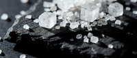 Coarse sea salt crystals scattered on dark slate stone, macro closeup with dramatic lighting for food and culinary backgrounds.