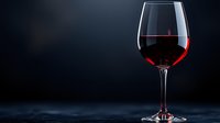 Glass of red wine on dark background with dramatic lighting and reflection, elegant composition for wine marketing and restaurant menus.