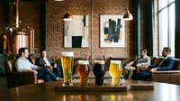 Diverse group of men enjoying craft beer and conversation in modern brewery taproom with exposed brick walls and industrial pendant lighting.