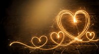 Golden light painting hearts with sparklers creating romantic glowing trails against dark background for Valentine's Day celebrations and love concepts.