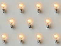 Glowing light bulbs arranged in rows on neutral gray background creating minimalist pattern of illuminated filaments for creative business concepts.