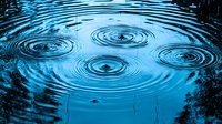 Concentric ripples forming symmetrical circles on blue water surface with droplets creating mesmerizing pattern of expanding rings in tranquil pond.