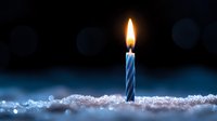 Single blue striped birthday candle with glowing flame on sparkling snow surface against dark background, creating magical winter celebration atmosphere.