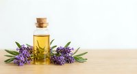 Lavender essential oil bottle with cork stopper and fresh purple lavender flowers on wooden surface for aromatherapy and natural wellness treatments.
