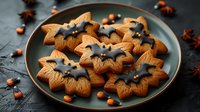 Star-shaped gingerbread cookies with dark chocolate glaze arranged on gray plate with hazelnuts and star anise scattered around on dark background.