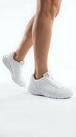 Close-up of female legs in white sneakers on neutral background. Athletic footwear and fitness lifestyle concept for sports and casual wear advertising.