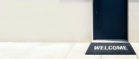 Black welcome mat placed in front of a dark door on a light tile floor, greeting visitors at a modern home entrance.