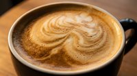 Overhead view of latte with latte art swirl in black mug on wooden surface, suitable for coffee shop menus, cafes, and beverage marketing.