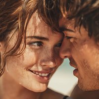 Young couple with freckles sharing intimate moment in golden sunlight. Romantic summer portrait of man and woman close together outdoors for lifestyle content.