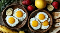 Fresh sunny side up eggs served in rustic wooden bowls with strawberries, banana slices, lemon and toasted bread on dark wooden background, healthy breakfast setting.