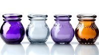 Colorful glass jars in purple, clear, lavender, and amber arranged in row on white background, perfect for storage or decorative use.