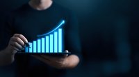 Person holding tablet displaying glowing blue growth chart with upward trend on dark background for business analytics and financial performance tracking.