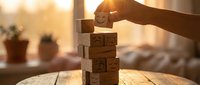 Hand placing wooden block with smiley face on stack of cubes in warm sunlight. Business growth, teamwork and positive mindset concept for motivation.