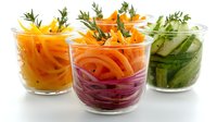 Fresh vegetable appetizers in glass cups with carrot, beet and cucumber spirals, garnished with herbs, served as healthy party snacks or restaurant starters.