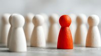 Red wooden pawn figure standing out among white pawns, symbolizing leadership, uniqueness, and differentiation in business or personal development.
