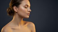 Serene young woman with closed eyes and natural makeup in profile view against dark background for beauty and wellness concepts.