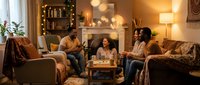 Young diverse friends enjoying cozy evening together in warm living room with fairy lights, sharing drinks and conversation on comfortable sofa.