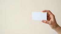 Male hand holding blank white business card against neutral beige background, suitable for branding, corporate identity, and marketing mockup designs.