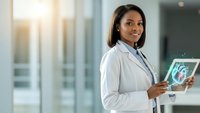 Professional African American female doctor in white coat holding digital tablet with medical imaging in modern hospital corridor with natural lighting.