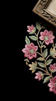 Elegant pink floral embroidery on black fabric with ornate wooden frame corner, showcasing traditional needlework craftsmanship and decorative textile art.