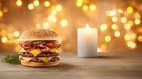 Double cheeseburger with melted cheese, bacon and fresh vegetables on wooden table against warm bokeh lights and white candle background for menu design.