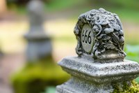 Stone cemetery marker with number 666 carved into aged monument, covered in moss and weathered texture against blurred natural background.