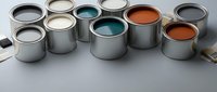 Open paint cans with colorful paint samples in teal, orange, white and gray colors arranged on white surface for home renovation projects.
