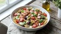 Mediterranean pasta salad with grilled chicken, cherry tomatoes, olives and fresh herbs in white bowl on rustic wooden table by sunny window.