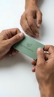 Two men with medium skin tone exchanging a green business card with leaf logo on white background, representing sustainable finance, eco-friendly investment, and corporate partnership in environmental business sector.