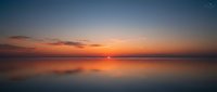 Serene sunset over calm water with golden and orange hues reflecting on mirror-like surface, peaceful nature landscape for relaxation and meditation projects.