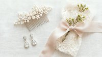 Elegant bridal accessories set with pearl hair comb, crystal earrings, lace garter and silk ribbon on white background for wedding day preparation.