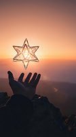 Hand holding geometric star shape against golden sunset sky with mountain landscape backdrop, symbolizing hope and spirituality.