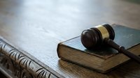 Wooden judge gavel resting on old law book with legal documents on rustic wooden desk for courtroom justice and legal proceedings.